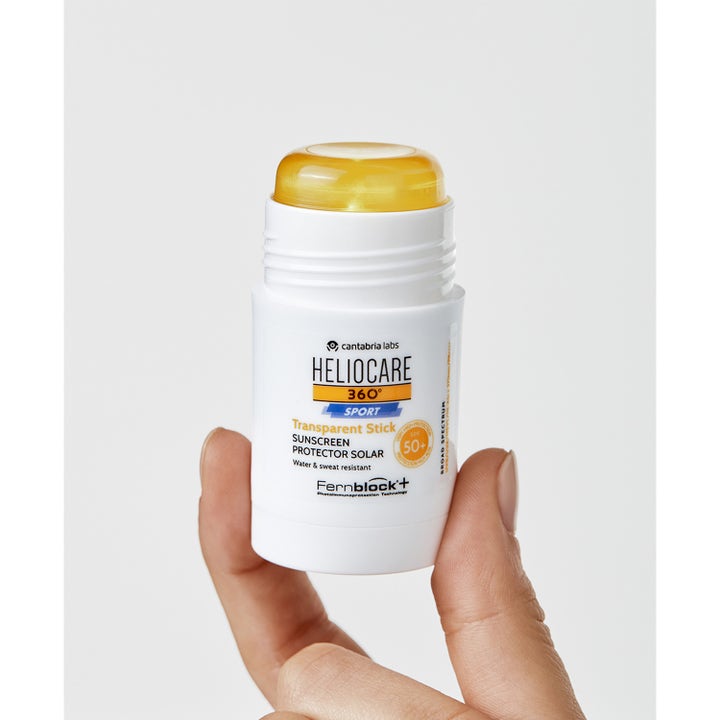 Heliocare Sport Stick SPF 50+ 25 g solskydd ansikte som hålls i en hand och visar det gula genomskinliga stiftet