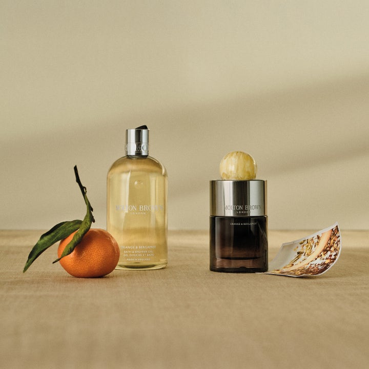Molton Brown Orange & Bergamot 300 ml lyxig duschtvål i genomskinlig flaska bredvid en orange apelsin med blad.