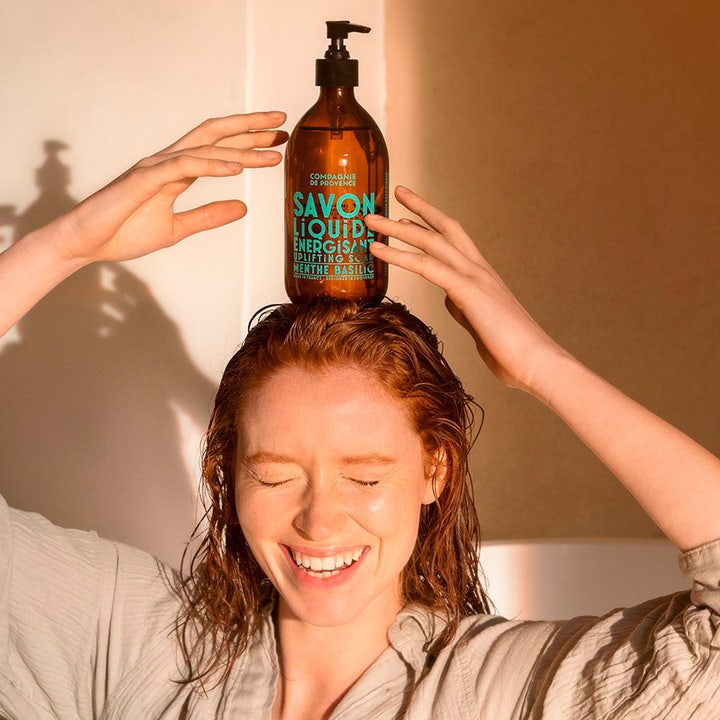 Compagnie de Provence Liquid Marseille Soap Mint Basil 495 ml fransk flytande tvål balanserad på en leende kvinnas huvud.