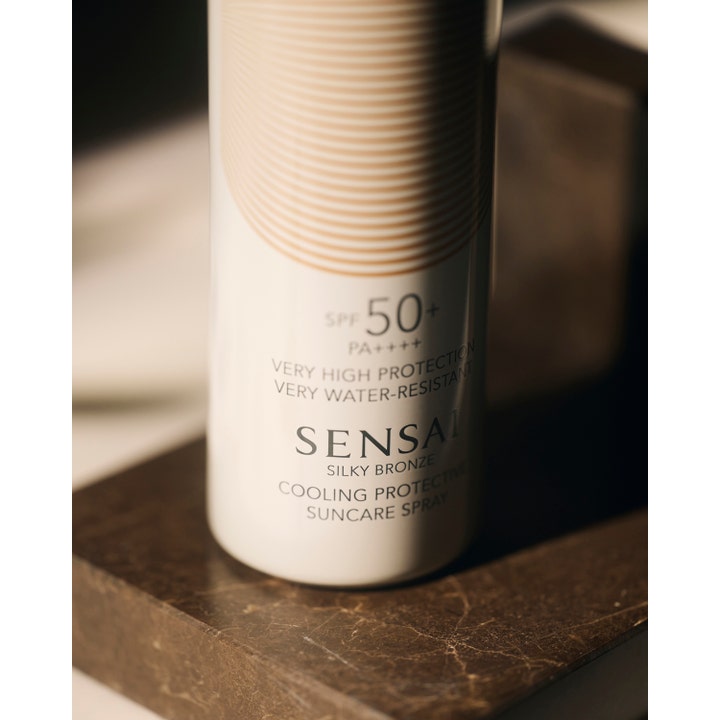 Sensai Silky Bronze Cooling Protective Suncare Spray 150 ml kylande solspray SPF 50+ i vit flaska på mörk sten.