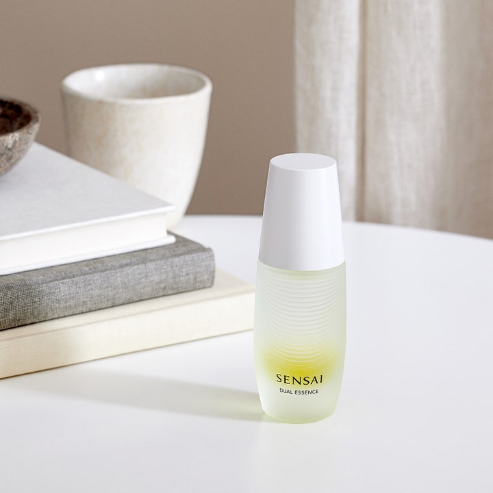 Sensai Dual Essence 30 ml dual återfuktande serum ger ansiktsglöd i en frostad flaska placerad vid böcker
