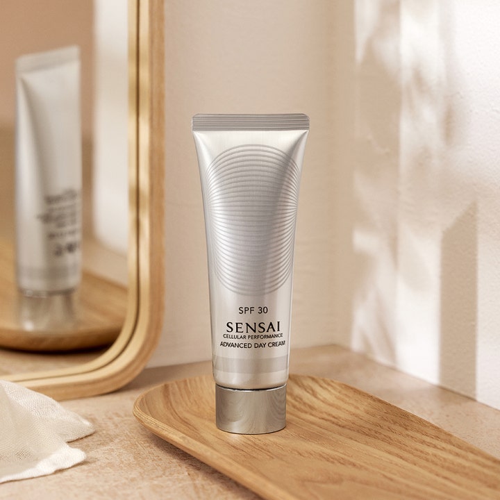 Sensai Cellular Performance Advanced Day Cream 50 ml dagkräm med spf 30 i en elegant silverfärgad tub vid en spegel.