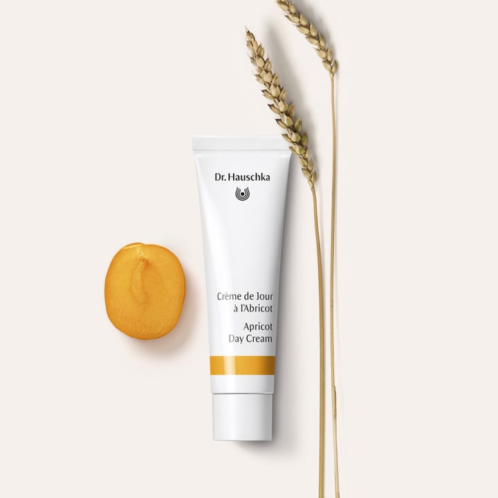 Dr. Hauschka Apricot Day Cream 30 ml lystergivande dagkräm i vit tub bredvid en aprikosskiva och veteax.