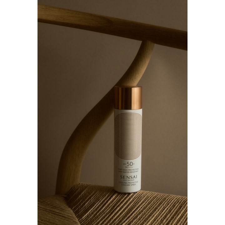 Sensai Silky Bronze Cooling Protective Suncare Spray SPF50 150 ml på flätad stol ger kylande solskydd