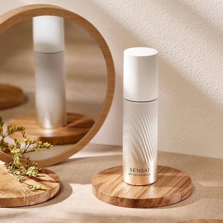 Sensai Lift Focus Essence 40 ml ansiktsessence lyfteffekt i räfflad pärlemorflaska placerad vid en rund spegel.