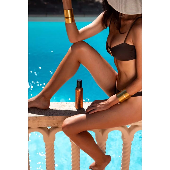 St.Tropez Instant Glow Body Bronzing Mousse 200 ml ger solkysst lyster bredvid en kvinna vid en klarblå pool