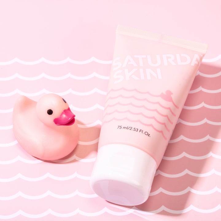 Saturday Skin Rub-a-Dub Refining Peel Gel 75 ml peeling i rosa tub bredvid en rosa gummianka på vågigt mönster.