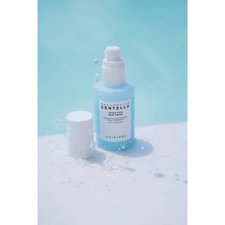 SKIN1004 Madagascar Centella Hyalu-Cica Blue Serum 50 ml i ljusblå pumpflaska omgiven av vattenstänk.