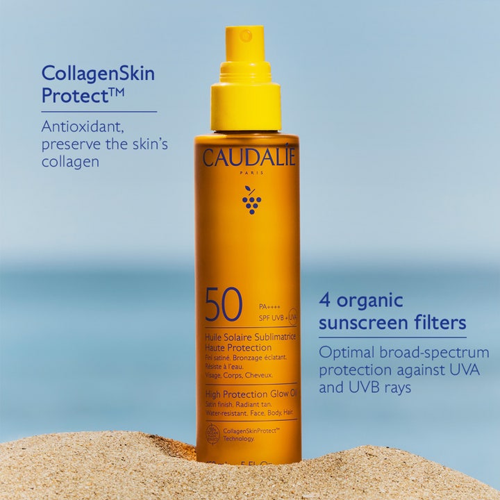 Caudalie Vinosun Glow Oil SPF50 150 ml solkräm med CollagenSkin Protect i orange flaska på en sandstrand vid havet.