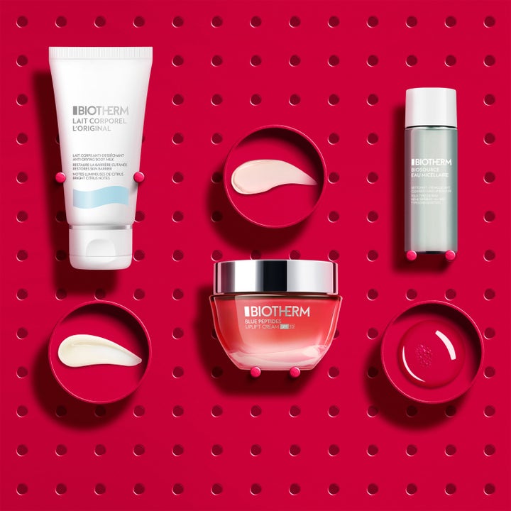 Biotherm Blue Peptides SPF30 Set hudvårdskit som ger fasthet med rosa glasburk, vit tub och texturer på röd bakgrund.