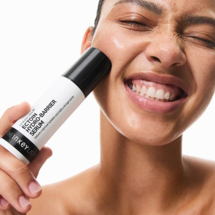 The INKEY List Ectoin Hydro-Barrier Serum 30 ml barriärstärkande serum i svartvit tub som hålls mot en persons kind.