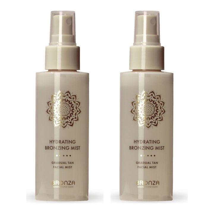 Bronza Hydrating Bronzing Mist ger gradvis lyster i två genomskinliga sprayflaskor med vita pumpar och gulddetaljer.