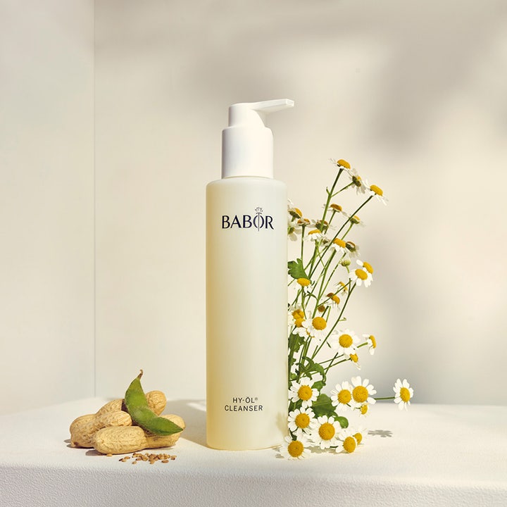 Babor HY-Öl Cleanser 200 ml oljerengöring ansikte i frostad pumpflaska omgiven av prästkragar och jordnötter.