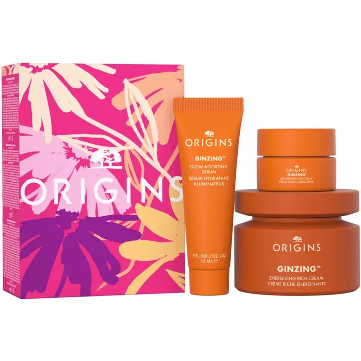 Origins GinZing hudvårdsset ger lyster med kräm, ögonkräm och serum i orange förpackningar bredvid blommig ask.