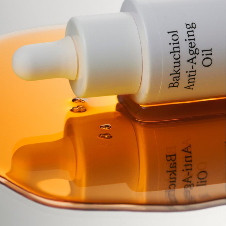 Jorgobé Bakuchiol Anti-Ageing Oil 30 ml ansiktsolja anti-age för känslig hud i vit flaska i en pöl av bärnstensfärgad olja.
