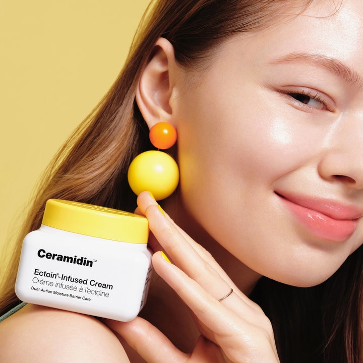 Dr.Jart+ Ceramidin Ectoin-Infused Cream 50 ml barriärstärkande ansiktskräm i vit burk med gult lock bredvid kvinna.
