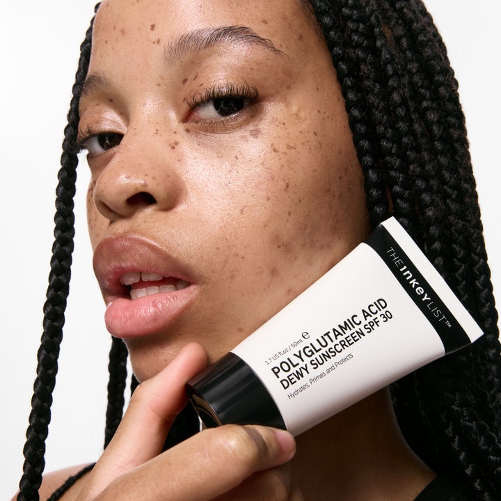 The INKEY List Polyglutamic Acid Dewy Sunscreen 50 ml återfuktande solkräm med polyglutaminsyra i vit tub mot en kind.