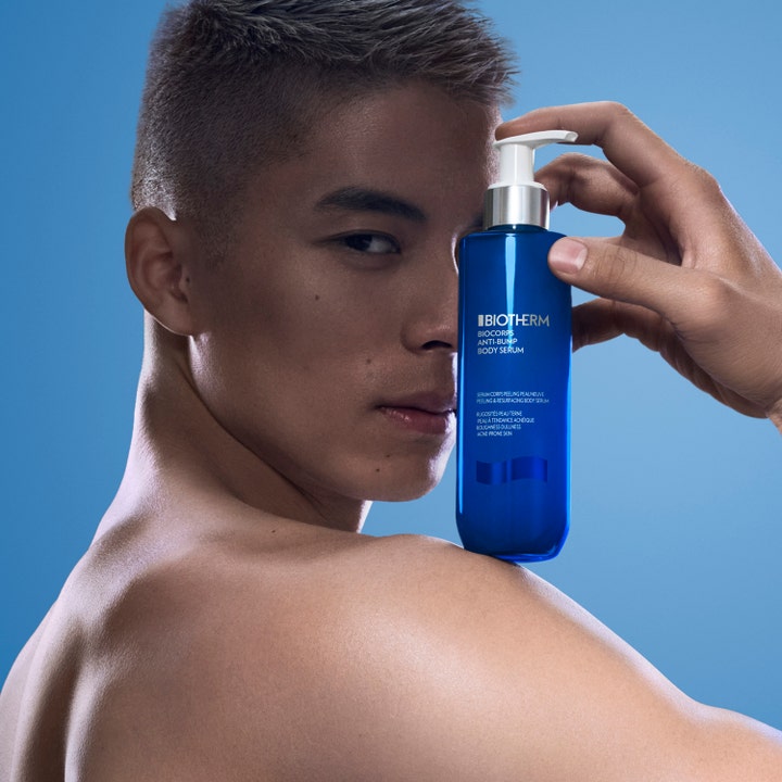 Biotherm Biocorps Body Serum 200 ml aknebehandling för kroppen i blå pumpflaska som hålls framför en mans ansikte.