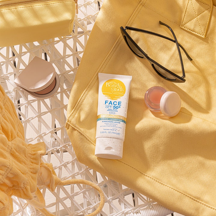 Bondi Sands SPF50+ Hydrating Tinted Face Lotion 75 ml fuktlotion i tub bredvid en gul väska och solglasögon.