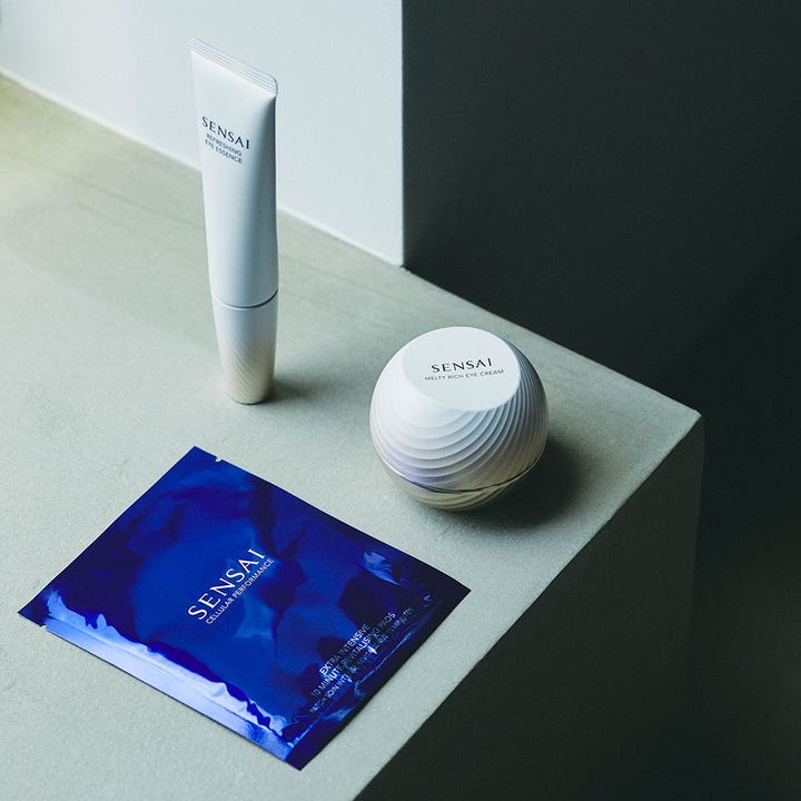 Sensai Total Eye Treatment 35 ml rynkreducerande set med vit tub, mönstrad burk och blått kuvert på grå yta.