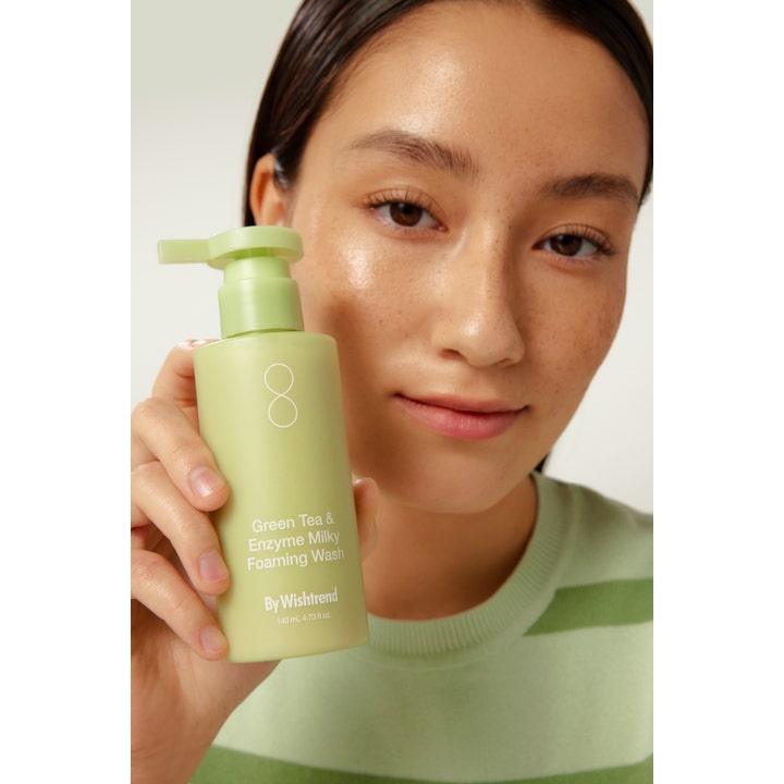 By Wishtrend Green Tea & Enzyme Milky Foaming Wash 140 ml ansiktsrengöring i ljusgrön pumpflaska som hålls av en kvinna.