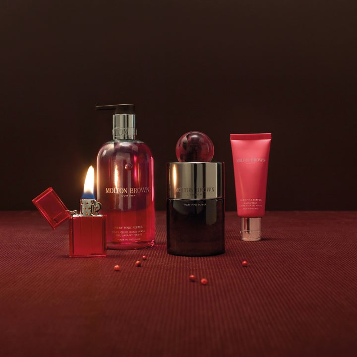 Molton Brown Fiery Pink Pepper 300 ml lyxig handtvål pump visas i miljö med tändare, handkräm och rosépeppar.