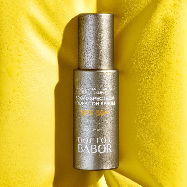 Babor DOC Hydration Serum 30 ml återfuktar med SPF 50+ i en silverflaska täckt av droppar mot gul bakgrund.