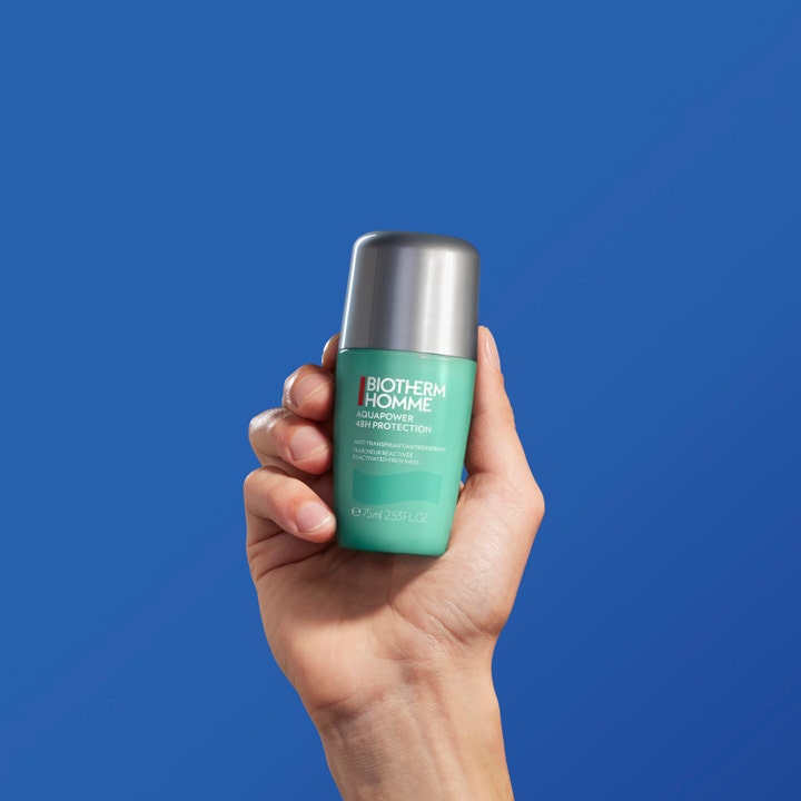 Biotherm Homme Aquapower 75 ml 48h antiperspirant ger en kylande effekt och hålls i en hand mot blå bakgrund.