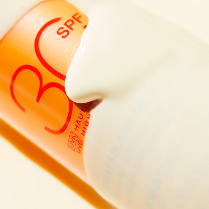 Nuxe Sun Spray SPF30 184 g anti-aging solskydd med krämig vit formula som rinner över den orange flaskan