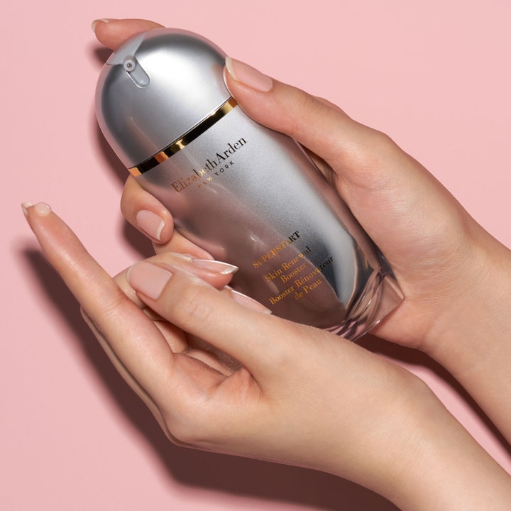 Elizabeth Arden Superstart Skin Renewal Booster 50 ml serum i silverflaska som hålls i händerna mot rosa bakgrund