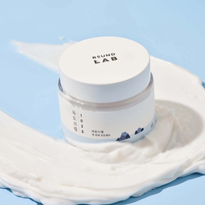 Round Lab 1025 Dokdo Cream 80 ml k-beauty fuktkräm ansikte i vit burk omgiven av mjuk vit krämtextur.