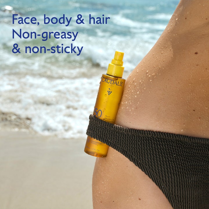 Caudalie Vinosun High Protection Glow Oil SPF50 150 ml sololja i sprayflaska på en strand vid havet