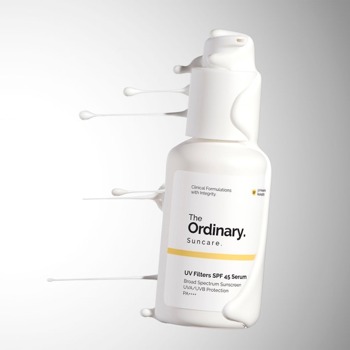 The Ordinary UV Filters SPF 45 Serum 60 ml är ett spf-serum i vit pumpflaska omgiven av krämiga vita droppar.