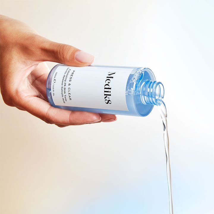 Medik8 Press & Clear 150 ml 2% BHA tonic hudvård som hälls ur en ljusblå flaska för Medik8 exfoliering.