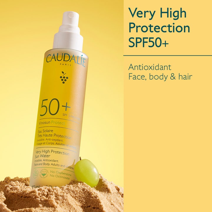 Caudalie Vinosun Very High Protection Water 150 ml SPF50+ solskyddsspray i gul flaska i sand med en grön druva