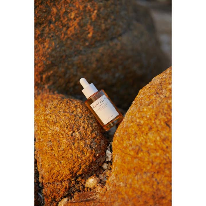 SKIN1004 Madagascar Centella Ampoule 55 ml lugnande cica ansiktsserum i glasflaska placerat på gyllene klippor.