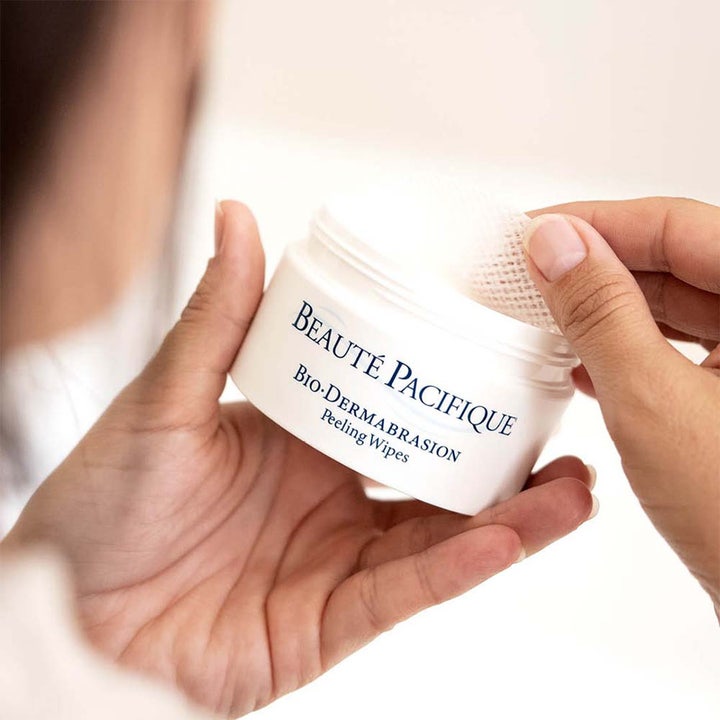 Beauté Pacifique Bio-Dermabrasion Peeling Wipes exfolierande pads i vit burk som lyfts upp av händer