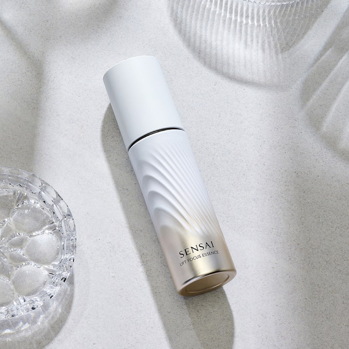 Sensai Lift Focus Essence 40 ml ansiktsessence lyfteffekt i vågformad vit och guldfärgad flaska på stenyta