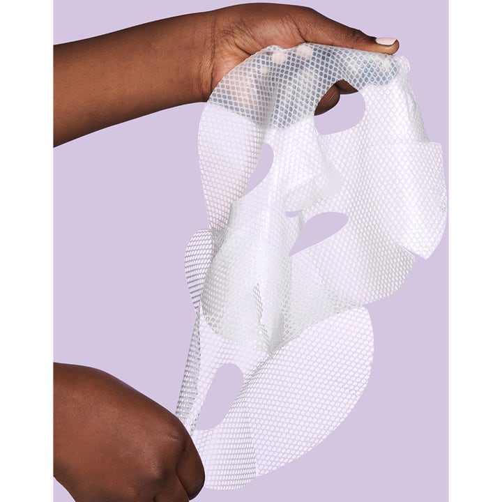 Exuviance Pick-Me-Up Plumping Mask 20 g sheet mask som hålls upp av händer mot lila bakgrund.