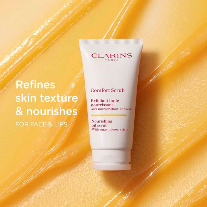 Clarins Comfort Scrub 50 ml närande ansiktsskrubb i vit tub på en bakgrund av gul textur med fina sockerkristaller.