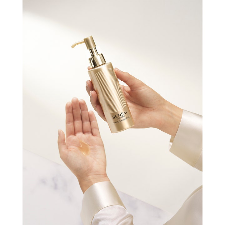 Sensai Ultimate The Cleansing Oil 150 ml rengöringsolja ansikte i guldflaska med pump och synlig oljetextur i handen