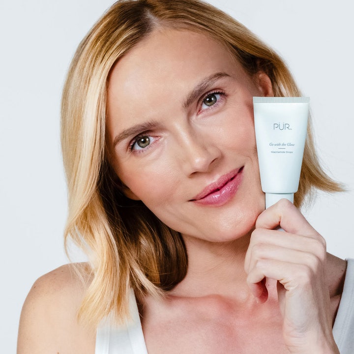 PÜR Go With The Glow Niacinamide Drops 30 ml lystergivande PÜR ansiktsserum i vit tub som hålls av en kvinna