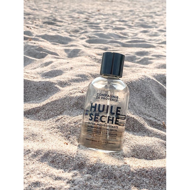 Compagnie de Provence Ultra Nourishing Dry Oil 100 ml närande torrolja med sheasmör i sanden på en strand.