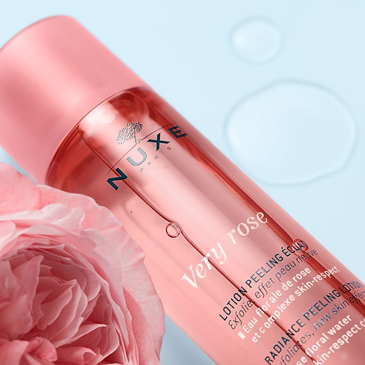 Nuxe Very Rose Peeling Lotion 150 ml ansiktspeeling för strålande hy bredvid en rosa ros och vattendroppar