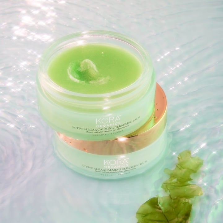 KORA Organics Active Algae Melting Cleansing Balm 100 g ekologisk sminkborttagning med grön textur och guldlock i vatten.