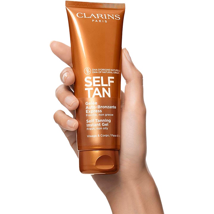 Clarins Self Tanning Instant Gel 125 ml ger lyster i en skimrande bronsfärgad tub som hålls av en hand.
