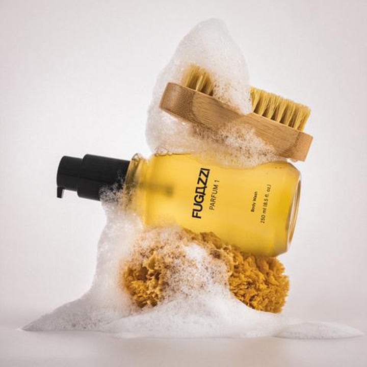 Fugazzi Parfum 1 Body Wash 250 ml rengörande duschtvål i pumpflaska omgiven av vitt skum, natursvamp och träborste.