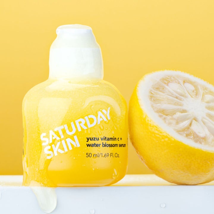 Saturday Skin Yuzu Vitamin C + Water Blossom Serum 50 ml lystergivande ansiktsserum i gul flaska bredvid en halv yuzufrukt.