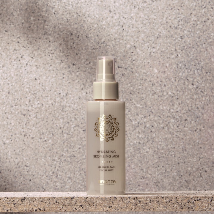 Bronza Hydrating Bronzing Mist Coconut 100 ml hydrerande solbrun ansiktsspray i beige flaska på en stenavsats