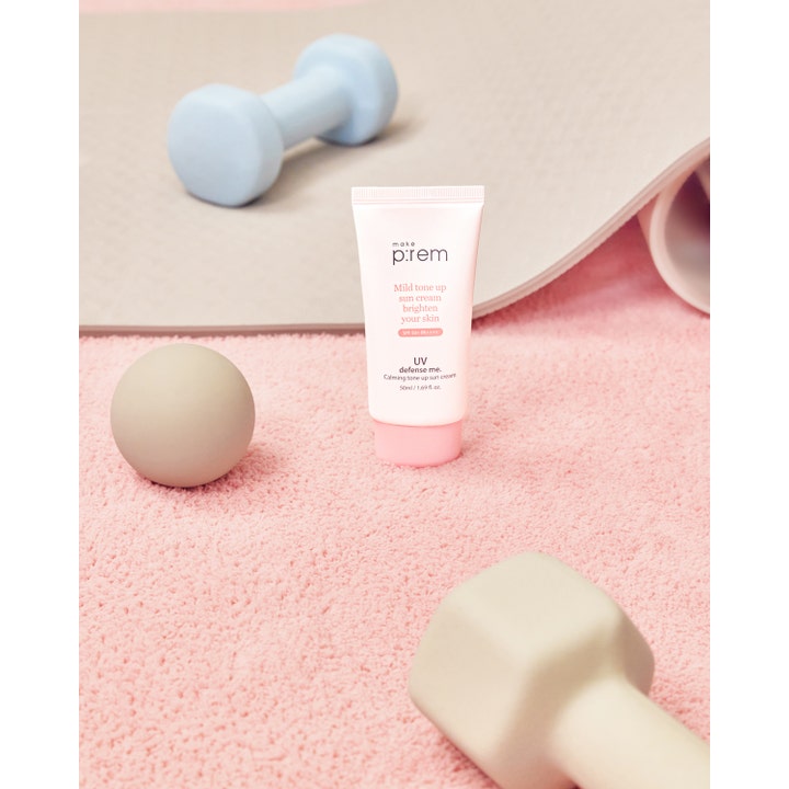 Make Prem UV Defense Me Calming Tone Up Sun Screen 50 ml ger uv-skydd i en rosa tub placerad bland hantlar och matta.
